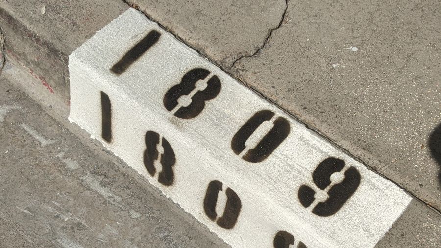 Freshly painted curb with a white reflective block and black numbers