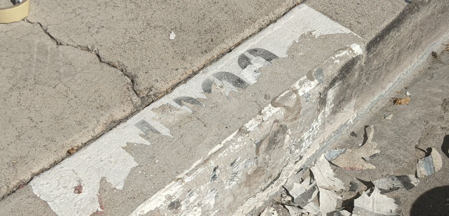 Curb with the old cracked paint scraped off, chips of old paint on the ground